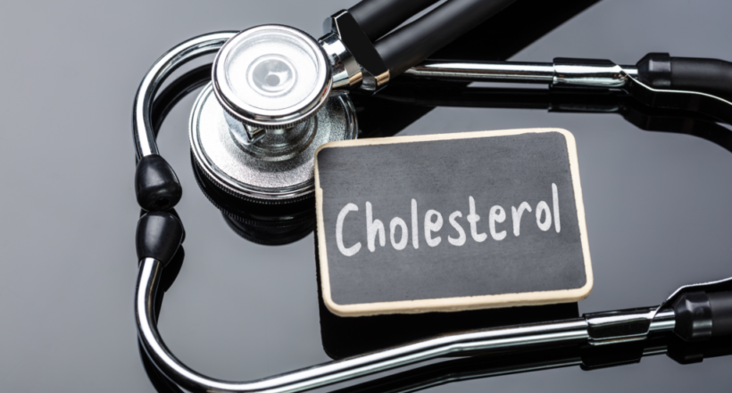 A stethoscope loops around a small chalkboard that reads “cholesterol,” for a post on how long it takes to lower cholesterol.