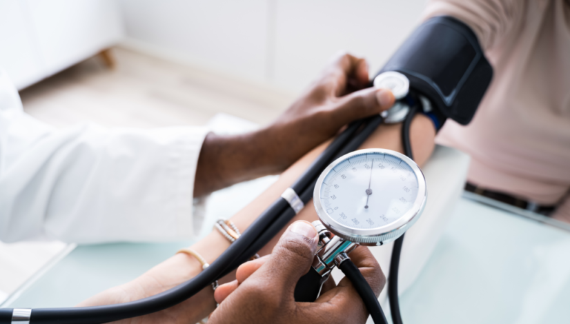 A doctor measures his patient’s blood pressure using a black blood pressure cuff and stethoscope.