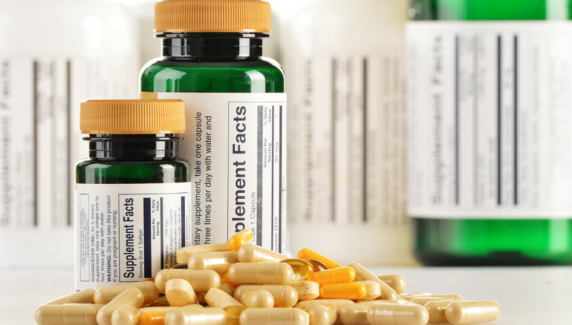A pile of various good quality supplement capsules are pictured in front of two dark green bottles with yellow lids.