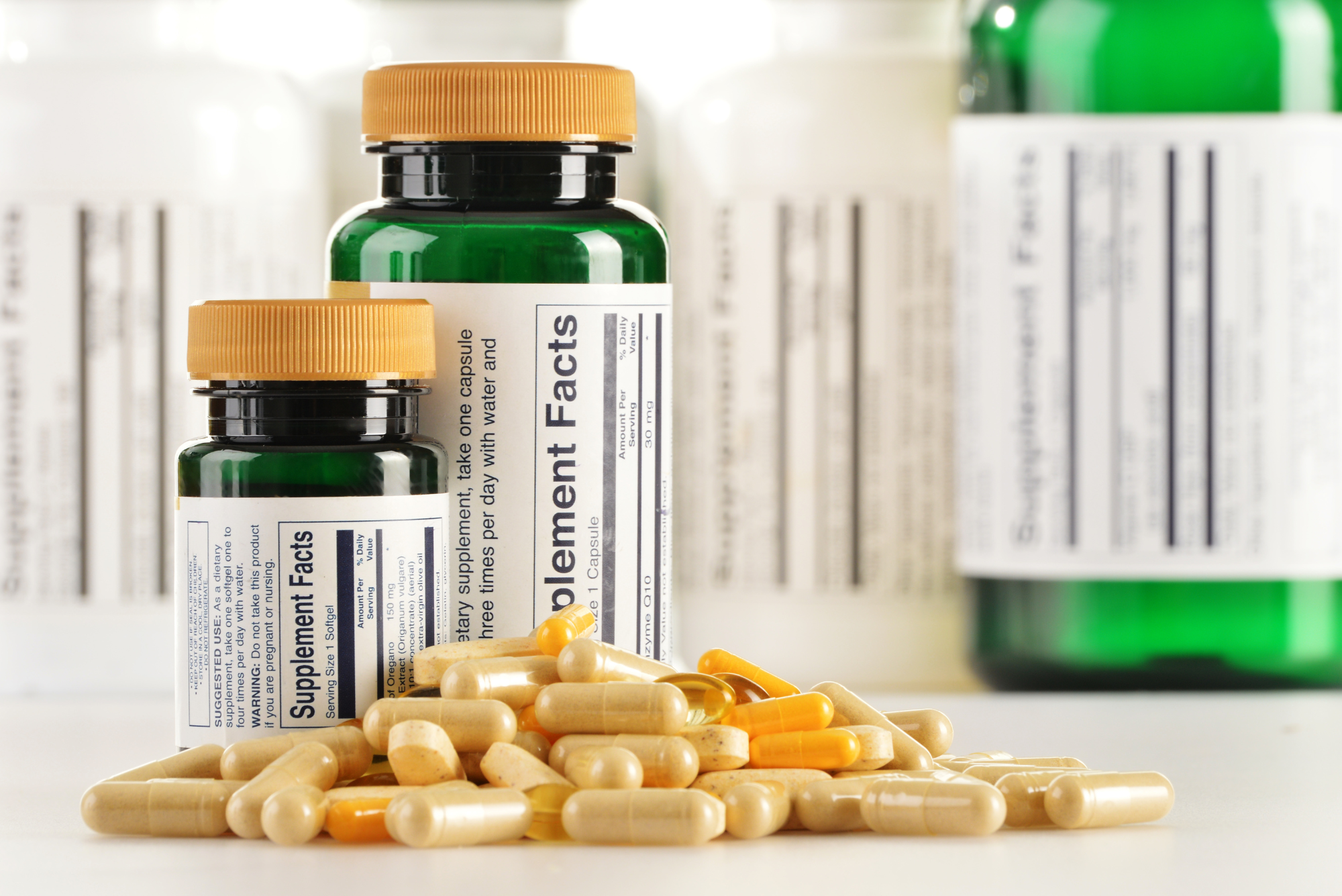 A pile of various good quality supplement capsules are pictured in front of two dark green bottles with yellow lids.