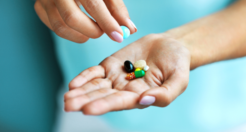 A woman who heard about supplements everyone should take holds out a handful of various colorful pills and capsules.