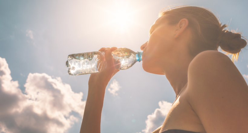 A woman drinks a bottle of water, the best way to hydrate, on a bright, sunny day.