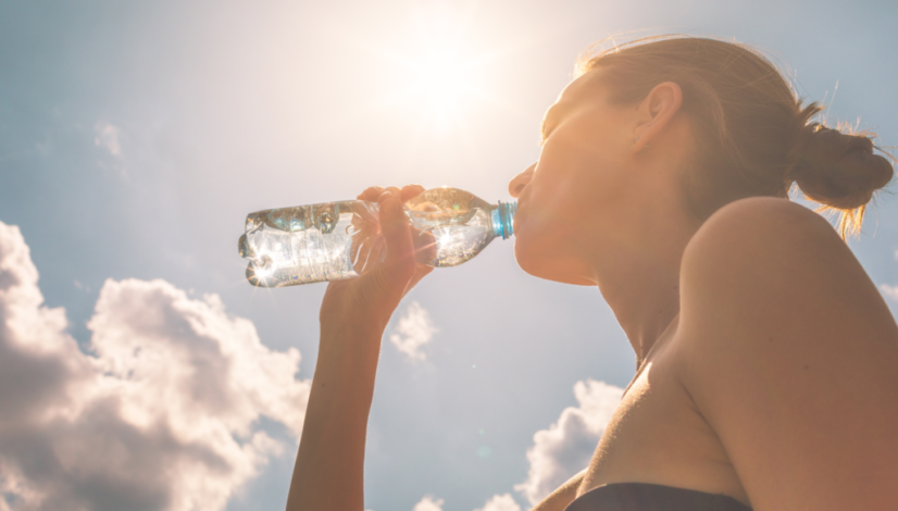 A woman drinks a bottle of water, the best way to hydrate, on a bright, sunny day.