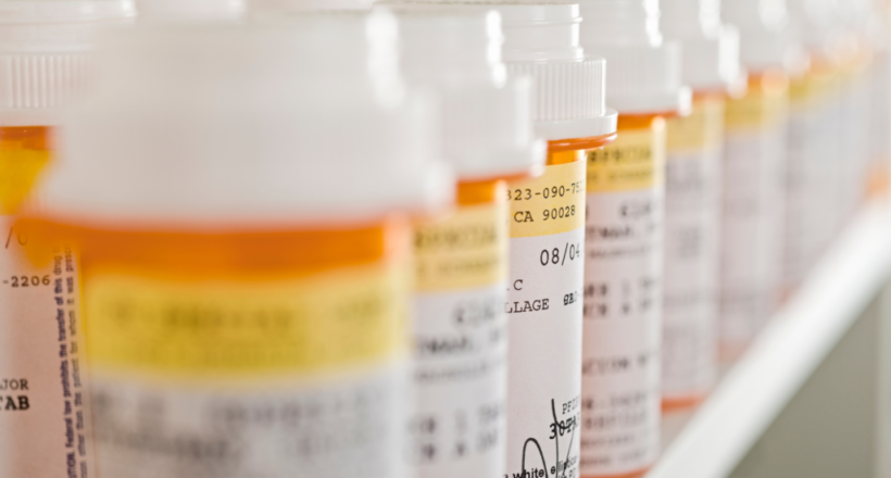 A row of orange pill bottles are lined up on a shelf, representing how to pay less for prescription drugs.