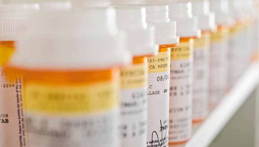 A row of orange pill bottles are lined up on a shelf, representing how to pay less for prescription drugs.