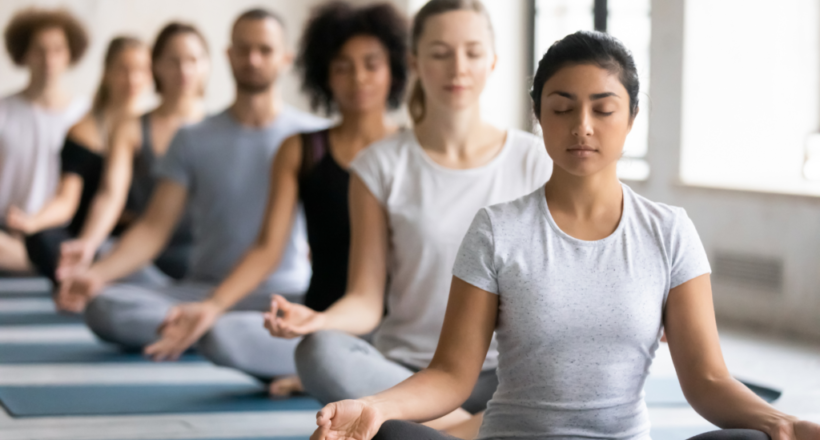 A group of people sitting cross-legged with eyes closed, practicing mindfulness and meditation.