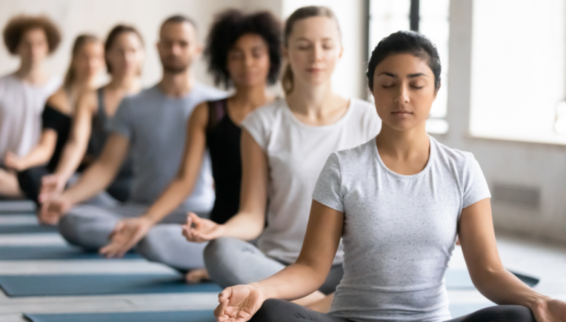 A group of people sitting cross-legged with eyes closed, practicing mindfulness and meditation.