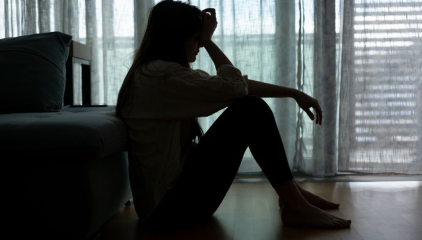 Silhouette of a woman sitting on the floor, holding her head in a dimly lit room, representing anxiety or depression.