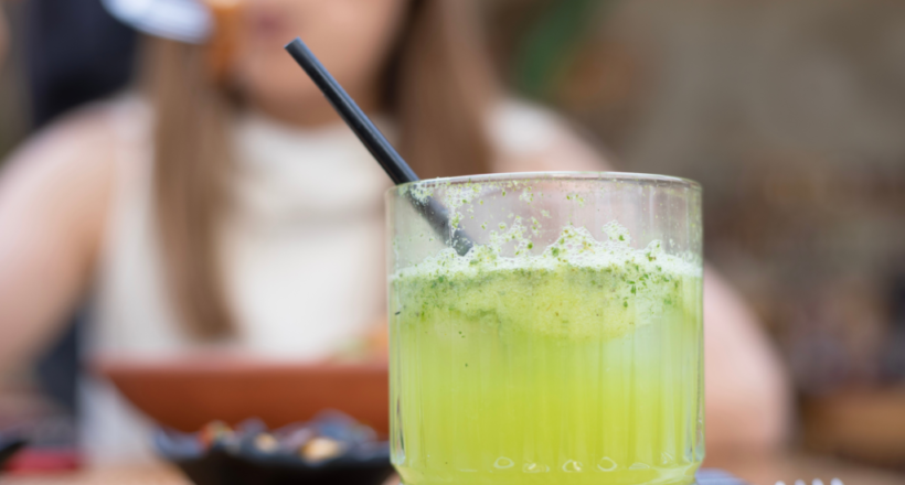 Close-up of a fresh green juice with foam and a black straw, showcasing a healthy antioxidant drink in a dining setting.