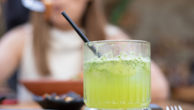 Close-up of a fresh green juice with foam and a black straw, showcasing a healthy antioxidant drink in a dining setting.