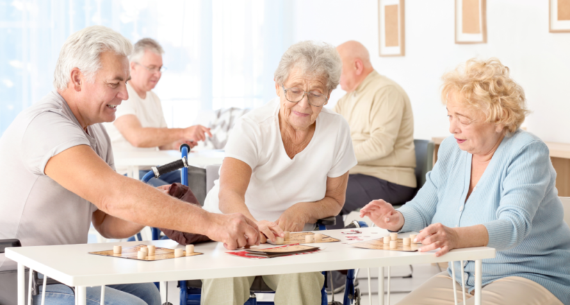 Senior adults playing board games together in a bright facility, promoting social interaction and engagement.