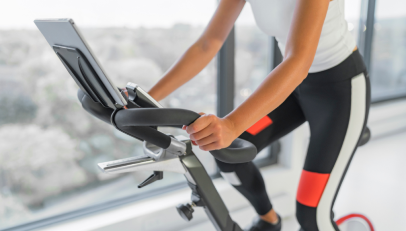 Person doing exercises on Peloton bike in white tank top and black-red leggings.