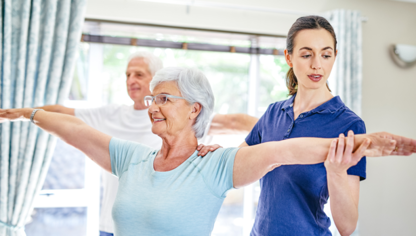 Physical therapist guides elderly woman and man doing arm exercises in a bright room.