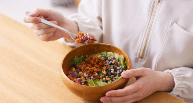 eat-enough-protein Person eating a healthy salad bowl with beans, lettuce, and plant-based protein at a wooden table.