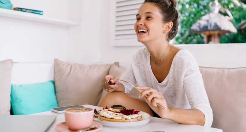 Smiling young woman sitting comfortably on couch, savoring a nourishing meal.