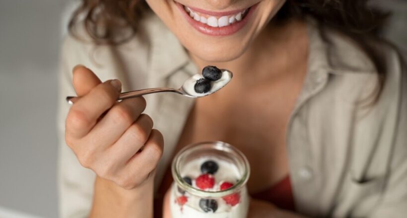 Smiling woman eating yogurt with blueberries.