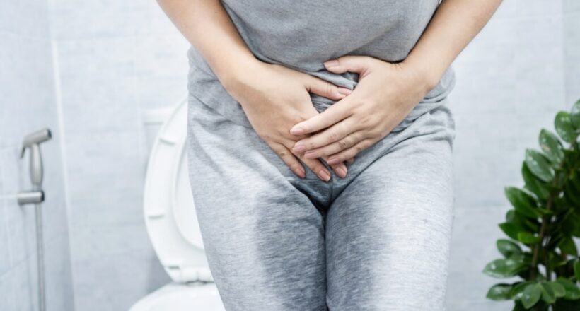 Person in gray clothing clasps hands over lower abdomen.