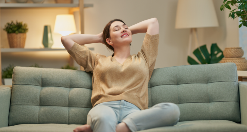 A woman relaxes contentedly on a couch, reflecting the calm benefits of environmental medicine.